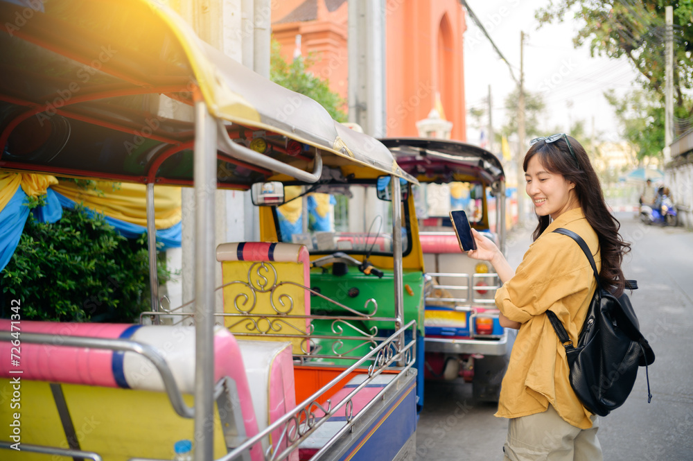 Obraz premium Young Asian woman backpack traveler standing a side of Tuk Tuk taxi on summer vacations at Bangkok, Thailand. Journey trip lifestyle, Asia summer tourism concept.