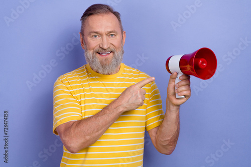 Portrait of optimistic person with beard wear yellow t-shirt indicating at megaphone announcing sale isolated on violet color background