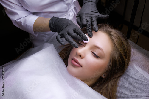 The master applies the cream to the model's eyebrows using a cotton sponge. PMU Procedure, Permanent Eyebrow Makeup.