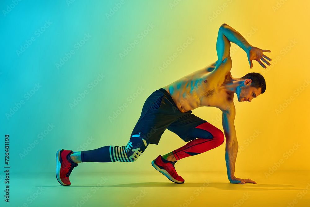 Grown strength and endurance. Muscular, athletic young man training shitless against gradient blue yellow background in neon light. Concept of active and healthy lifestyle, sport, fitness