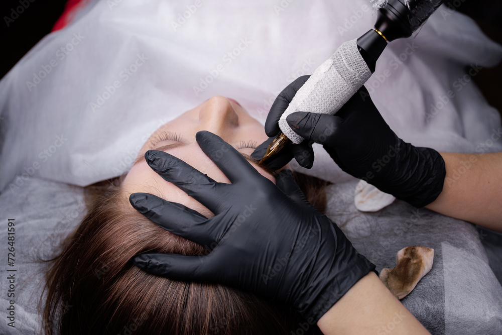 In the hands of the tattoo master is a machine in which a cartridge is inserted that applies pigment to the skin of the eyebrows. PMU Procedure, Permanent Eyebrow Makeup.