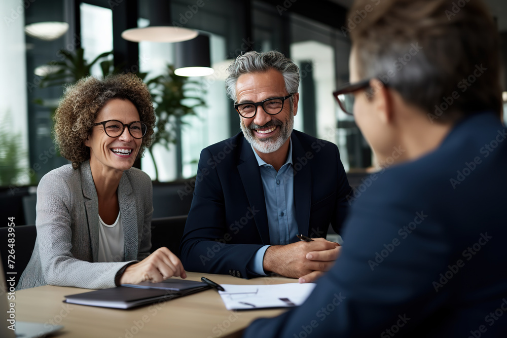 Middle-aged business colleagues in a meeting, sharing laughs while casually discussing business matters. Middle-aged business colleagues in a meeting, sharing laughs while casually discussing business matters.