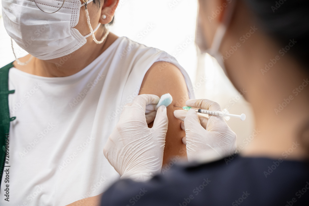 People getting a vaccination to prevent pandemic concept. Mature Woman in medical face mask  receiving a dose of immunization coronavirus vaccine from a nurse at the medical center hospital - obrazy, fototapety, plakaty 