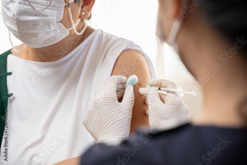 People getting a vaccination to prevent pandemic concept. Mature Woman in medical face mask  receiving a dose of immunization coronavirus vaccine from a nurse at the medical center hospital photo