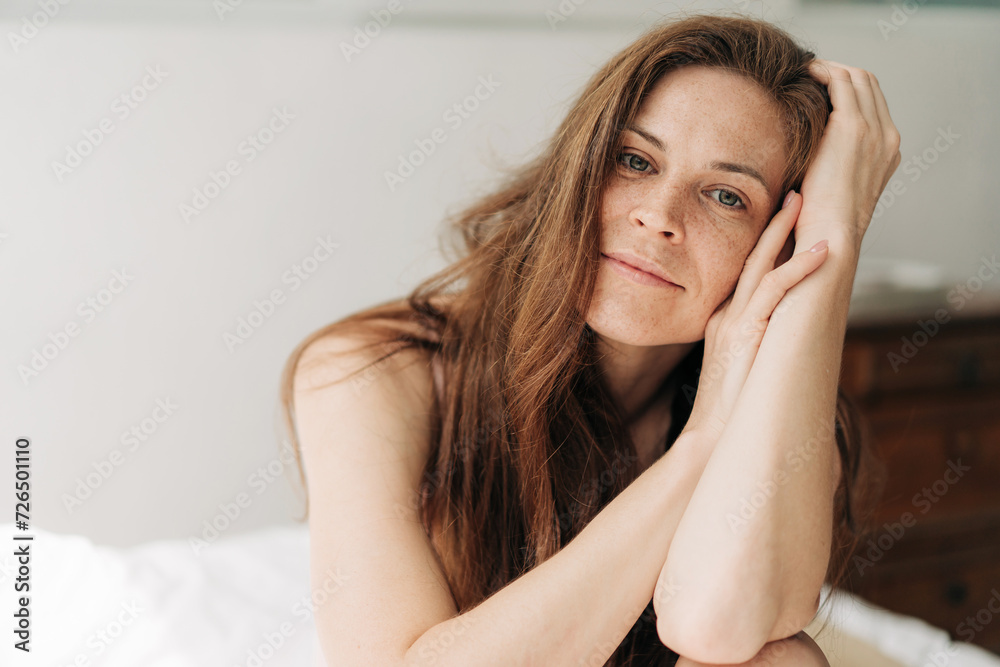 Portrait of a beautiful pensive freckled woman sitting on her bed in the morning. Portrait of a beautiful pensive freckled woman sitting on her bed in the morning.