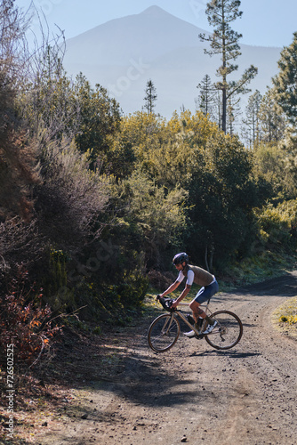 Fit male cyclist riding a gravel bike a gravel road with view on Teide volcano. Cyclist training on beautiful forest trail. Sport motivation. Adventure travel on bike. Tenerife, Canary Island.