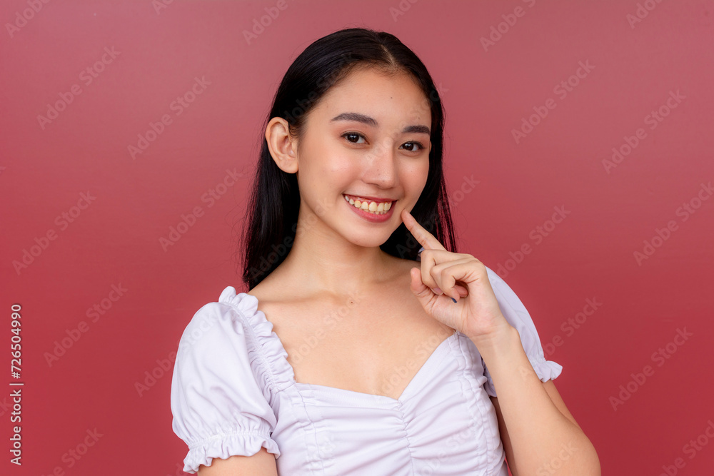 Portrait of a joyful young Asian woman with a charming smile, posing casually against a rich red backdrop. Portrait of a joyful young Asian woman with a charming smile, posing casually against a rich red backdrop.
