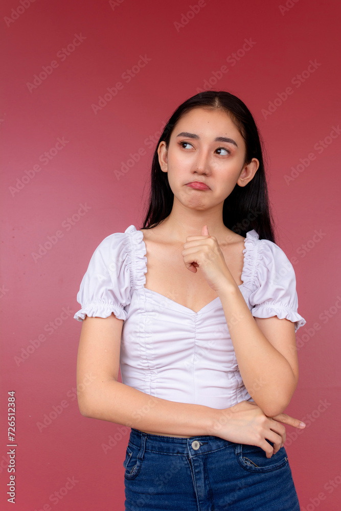 A pretty young asian woman in her early 20s having an internal debate, looking to the left while pondering. Studio shot with burgundy background. A pretty young asian woman in her early 20s having an internal debate, looking to the left while pondering. Studio shot with burgundy background.