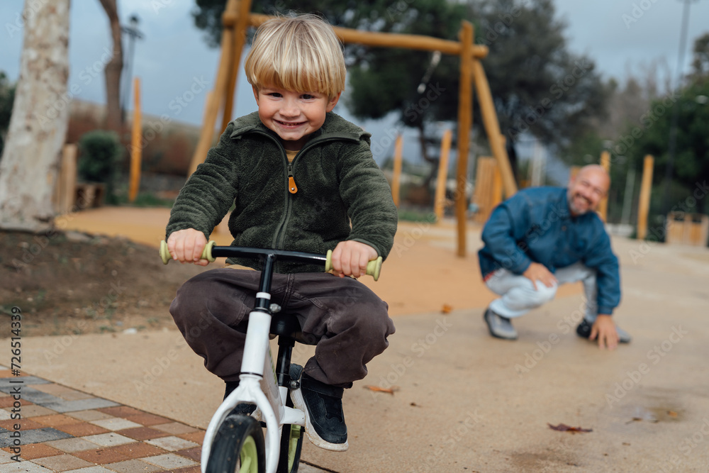 Dad teaches his son riding on bicycle in park. Father and son smile and have fun together Dad teaches his son riding on bicycle in park. Father and son smile and have fun together