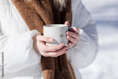 Woman drinking cup of hot tea or coffee outdoors in sunlight in cold winter day. Valentine day