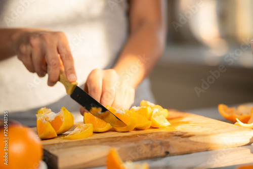 Close up shot of woman slicing oranges of making juice at morning in kitchen - concept of healthy lifestyle, nutrition and refreshing. photo
