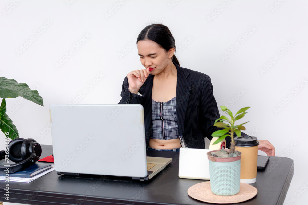 A young female office worker coughs while engrossed in her task at a desk with a laptop, coffee and office supplies. A young female office worker coughs while engrossed in her task at a desk with a laptop, coffee and office supplies.