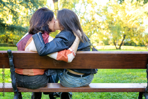 two unrecognizable women kissing on a public park bench. photo with copy space photo