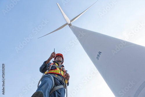 maintenance engineer standing  against turbines on wind turbine farm.