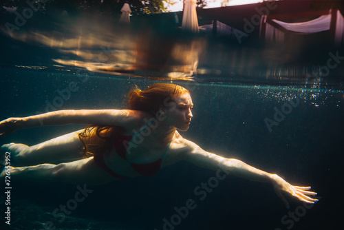 Canvas Print Young redheaded woman swimming underwater in a pool.