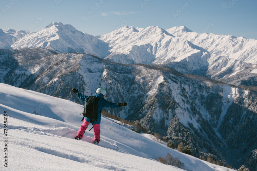 female snowboarder riding on slope of powdery snow in high mountains. Freeride at ski resort, amazing mountain peaks skyline