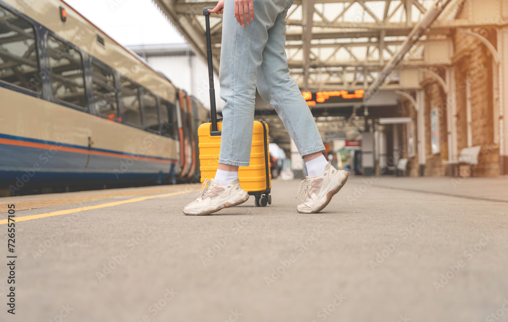 Obraz premium Traveler with a yellow suitcase waiting for a train at the train station on the platform. Travel concept.