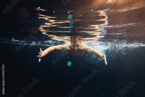 A young man swims in a pool, underwater. Concept of vacation and carefree life.