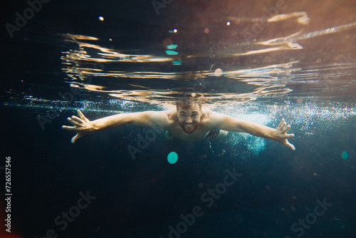 A young man swims in a pool, underwater. Concept of vacation and carefree life.