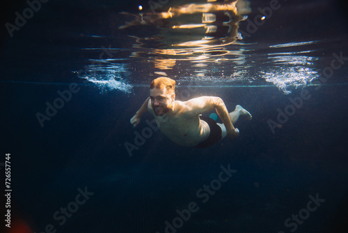 A young man swims underwater in a pool. Summer vacation concept.