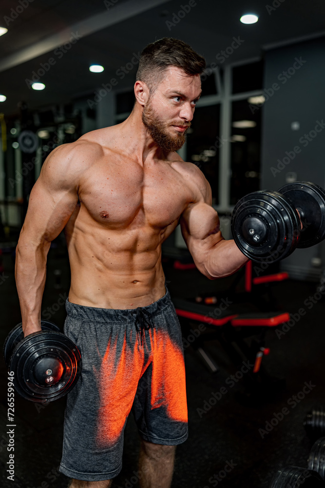 Muscular man trains his biceps with dumbbells in the gym.