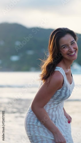Happy cheerful girl jumping on water sandy beach summer day. Attractive woman running on ocean and laughing to camera. Smiling cheerful lady have fun on seashore enjoy beautiful nature. Vertical
