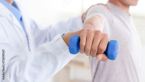 Doctor or Physiotherapist helping man exercise with dumbbell and physical therapy help for muscle or arthritis exercise in consulting exam. Doing the Rehabilitation therapy pain in clinic.