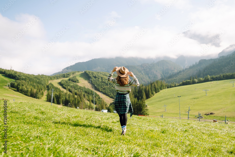 Woman walking on through green grass valley on background big mountains. Hiker resting. Beautiful National park. Fashion, beauty, tourism, resting concept.