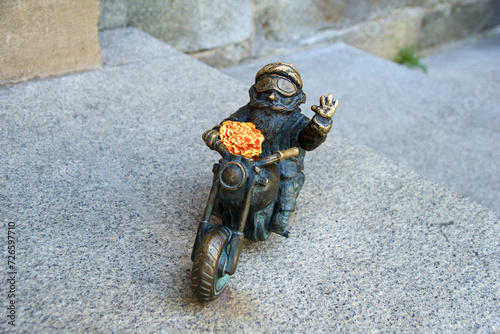 Fototapeta Naklejka Na Ścianę i Meble -  WROCLAW, POLAND - 16 JUN 2018: One of Wroclaw's gnomes on a motorbike. The bronze figures dwarfs are around 30 cm tall and are placed throughout the city centre of Wroclaw