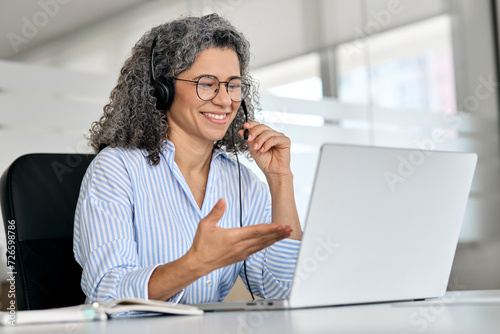 Happy mature business woman call centre representative customer support agent talking to client, smiling middle aged senior female operator wearing headset working using laptop computer in office. photo