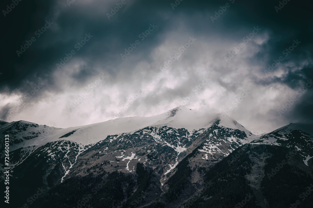 Beautiful mountain landscape. Clouds in the sky. Green grass. Snow on mountain peaks.
