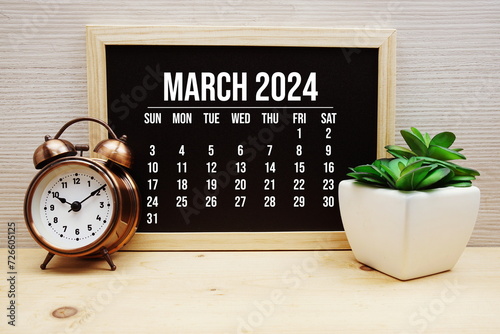 March 2024 monthly calendar and alarm clock on wooden background photo