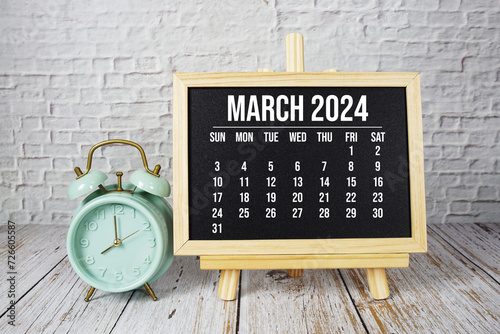 March 2024 monthly calendar and alarm clock on wooden background