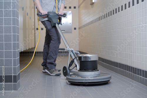 unrecognizable woman cleaning a washhroom floor with a buffer machine