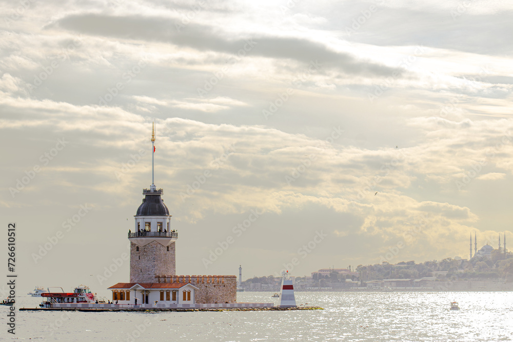 The Maiden's Tower basks in the soft glow of sunlight against a backdrop of Istanbul's skyline and sparkling Bosphorus waters, a serene moment in the city's vibrant life.