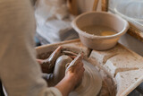 Close-up view of a potter's hands meticulously shaping a clay pot on a spinning wheel, with tools and water bowl nearby
