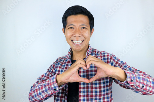 Young asian man isolated on white background smiling and gesturing a heart shape with hands