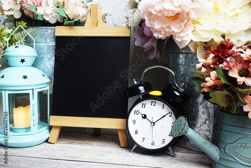 Easel mockup with blue landtern, alarm clock and flowers bouquet decoration on wooden background photo