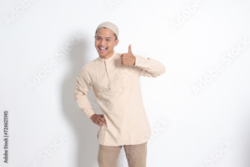 Portrait of attractive Asian muslim man in koko shirt showing thumb up, good job hand gesture. Approval concept. Isolated image on white background