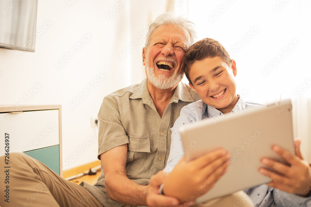 Cheerful grandpa and grandson using tablet PC at home
