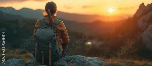 Back view young woman wearing a backpack and sit on stone in mountain at sunset. AI generated image photo