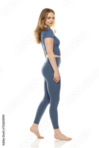 Full body, side view young woman in sportswear walking on white background