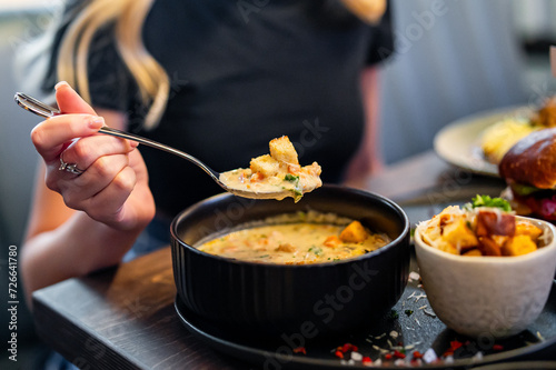 woman eating vegetable fish cream soup in bowl at cafe or restaurant