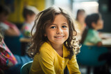 Smiling girl child sitting at desk in elementary school classroom with blurry students in background