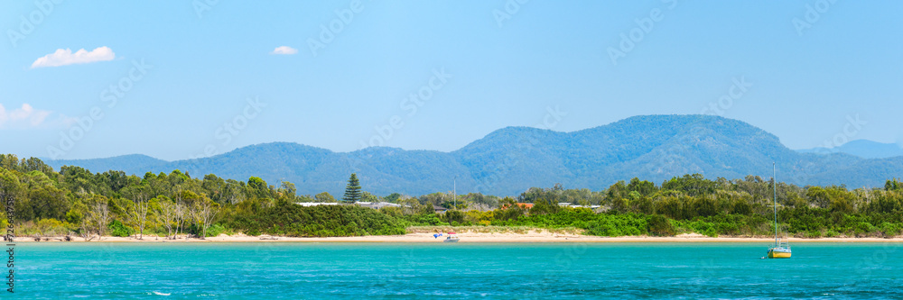Australian coast, seaside landscape with blue water, sandy shore and mountains in the background, summer sunny day.