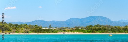 Australian coast, seaside landscape with blue water, sandy shore and mountains in the background, summer sunny day.