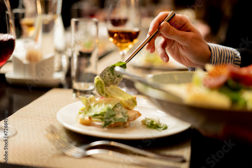 close-up of a person in a restaurant putting a salad on a plate on a servery table photo