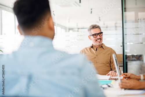 A confident mature male professional involved in discussion with colleagues, suggesting a scenario of leadership and mentoring, a culture of shared knowledge and growth