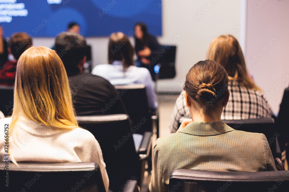 © tsuguliev - Female participants audience at the symposyum meeting, attendees in conference room hall listens to lecturer, group of women on a congress together listen to speaker on a stage at master-class