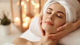 A woman with white towel turban on head relaxing and enjoying facial treatment at the spa gets a facial massage